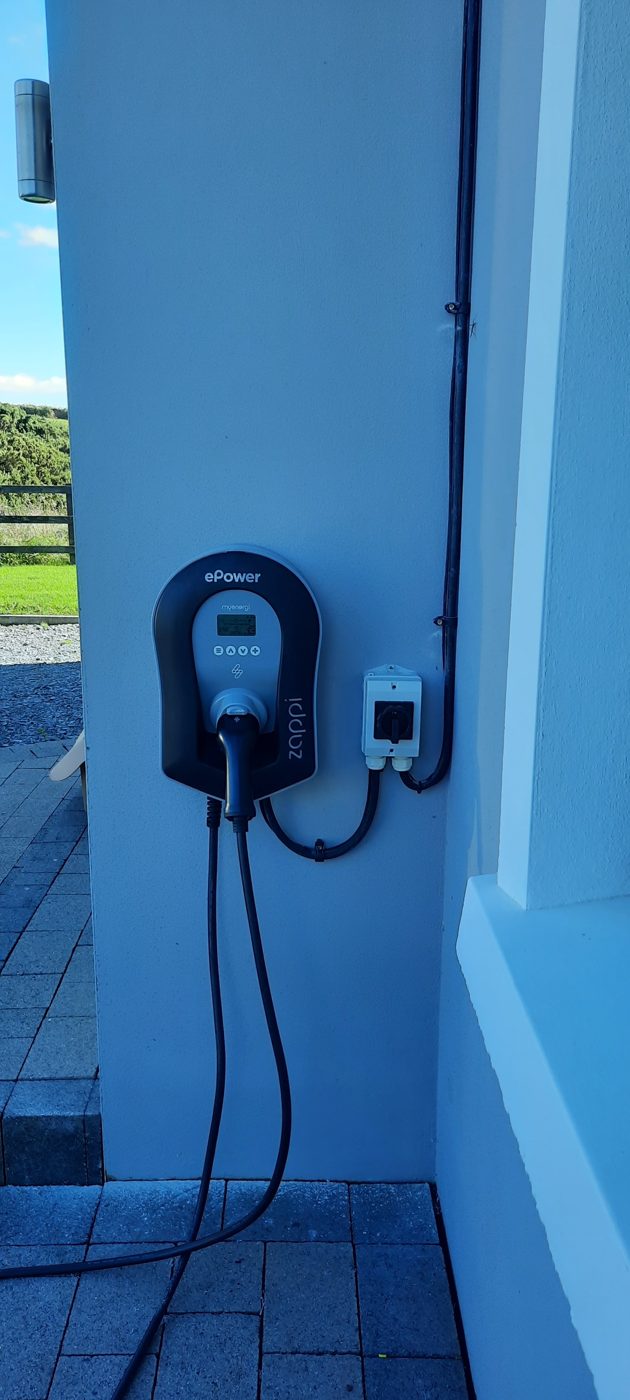 An EV charger and isolator on a blue painted wall, the cable hanging in a loop