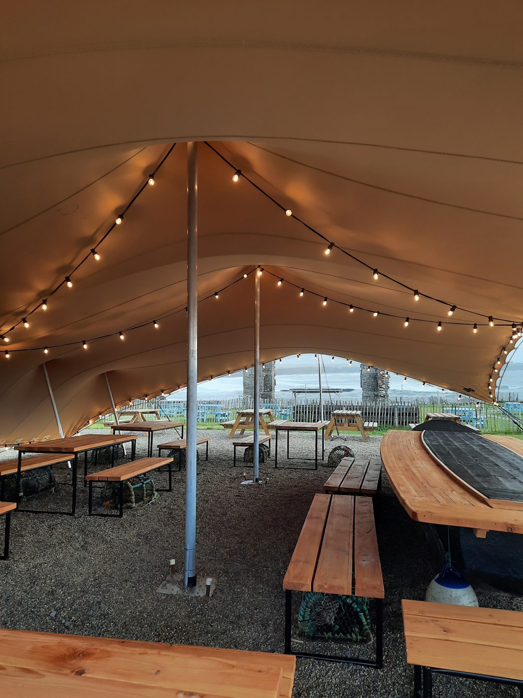 Festoon lights strung under a white marquee roof over long wooden benches