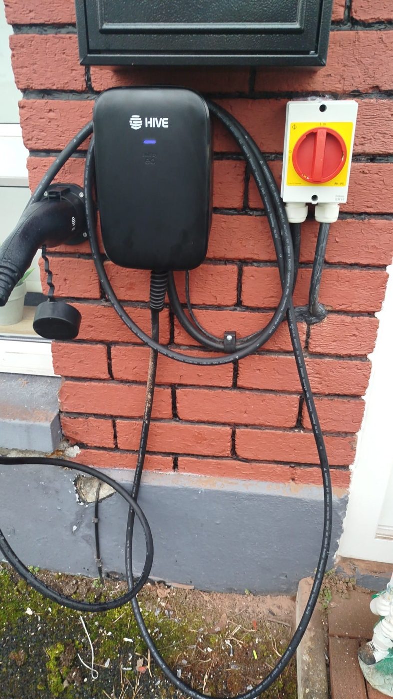 A Hive EV charger and a yellow rotary isolator on a red brick wall